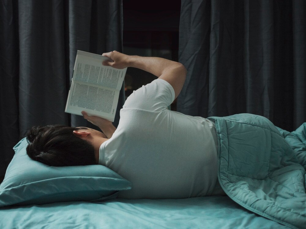 A portrait of man reading a book while laying on bed.