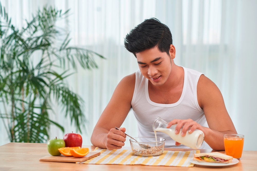 A portrait of man pouring milk into a bowl of oatmeal.