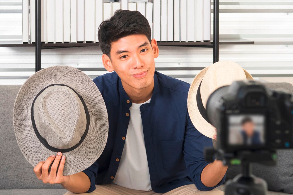 A portrait of man showing two different hats in front of the camera.