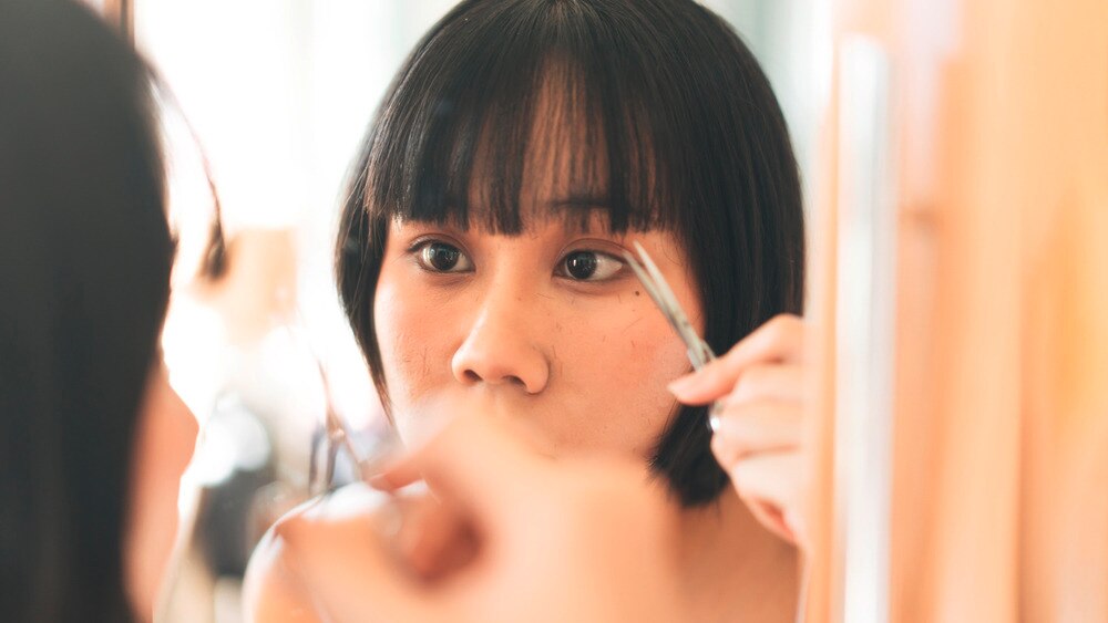 A portrait of woman cutting her bangs in front of the mirror.
