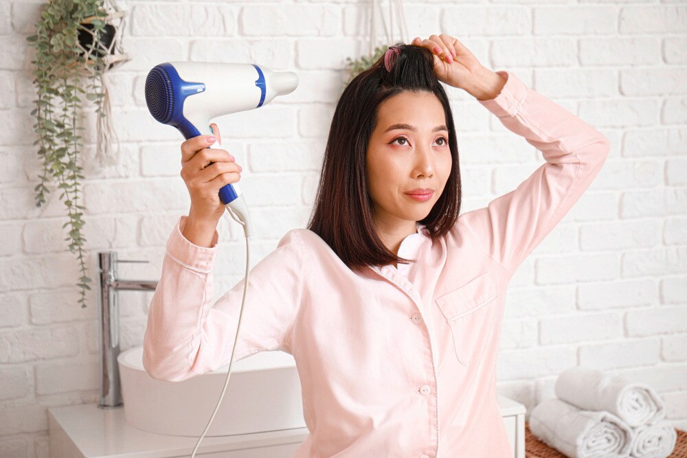 A portrait of woman blow-drying her bangs.