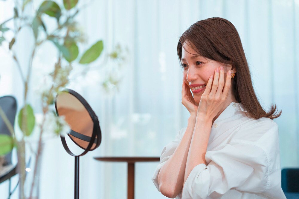 A portrait of woman touching her cheeks while looking at her reflection in the mirror.