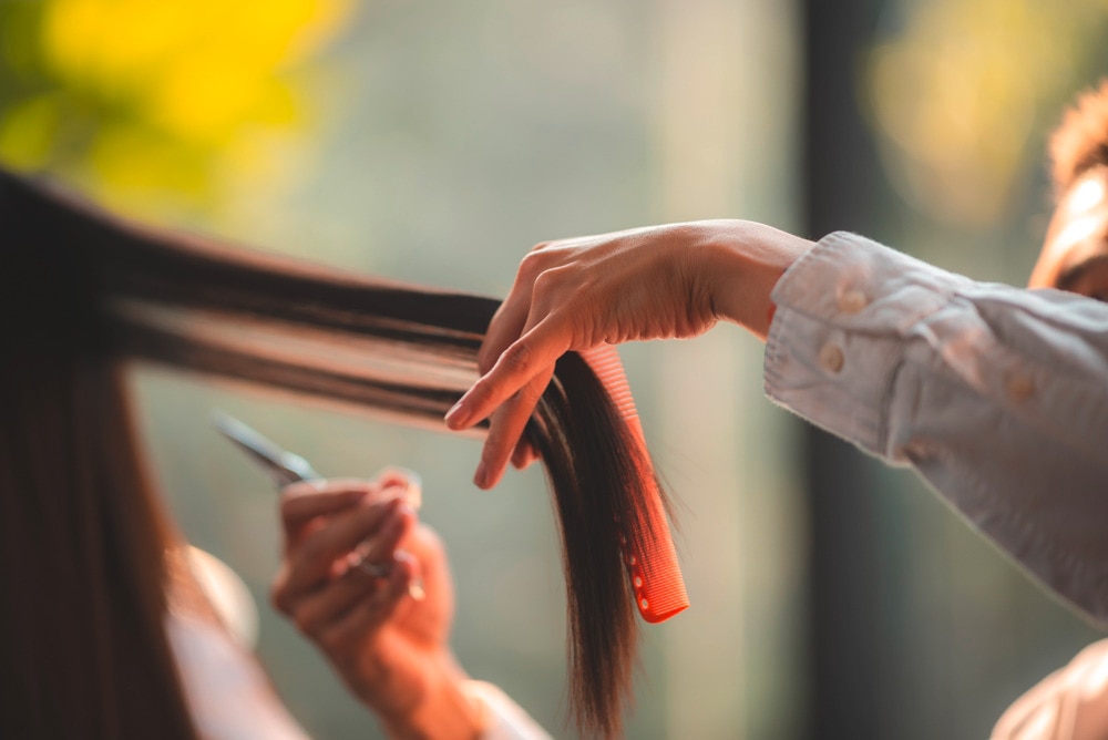 A hairdresser combing a woman’s long hair before cutting it.