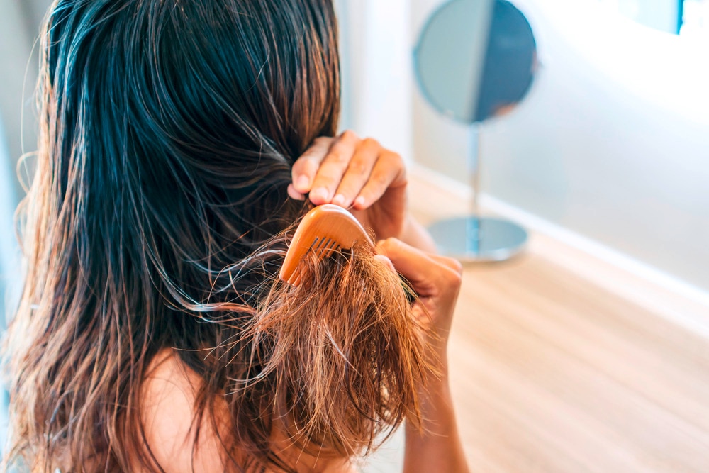 Woman brushing her knotty hair with wooden brush.