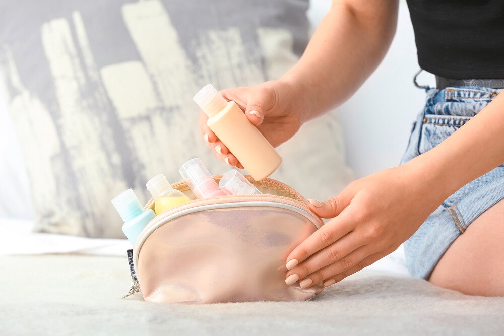 Woman packing travel cosmetic bottles into pouch.