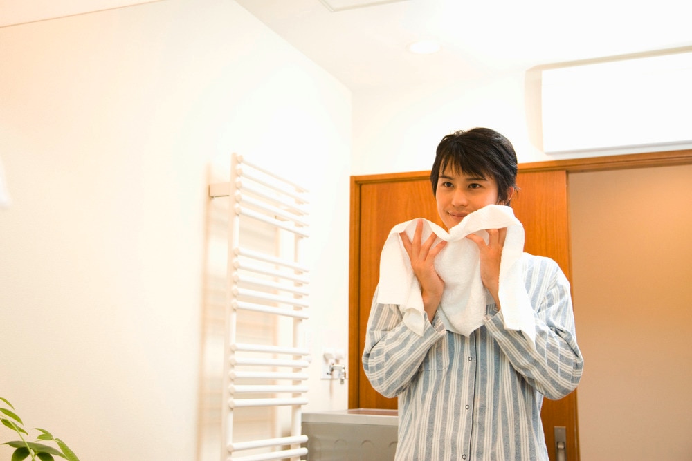 Young Asian man wiping face with towel.