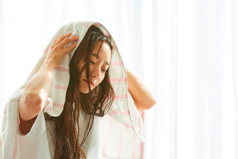 A portrait of woman drying her hair with a towel.