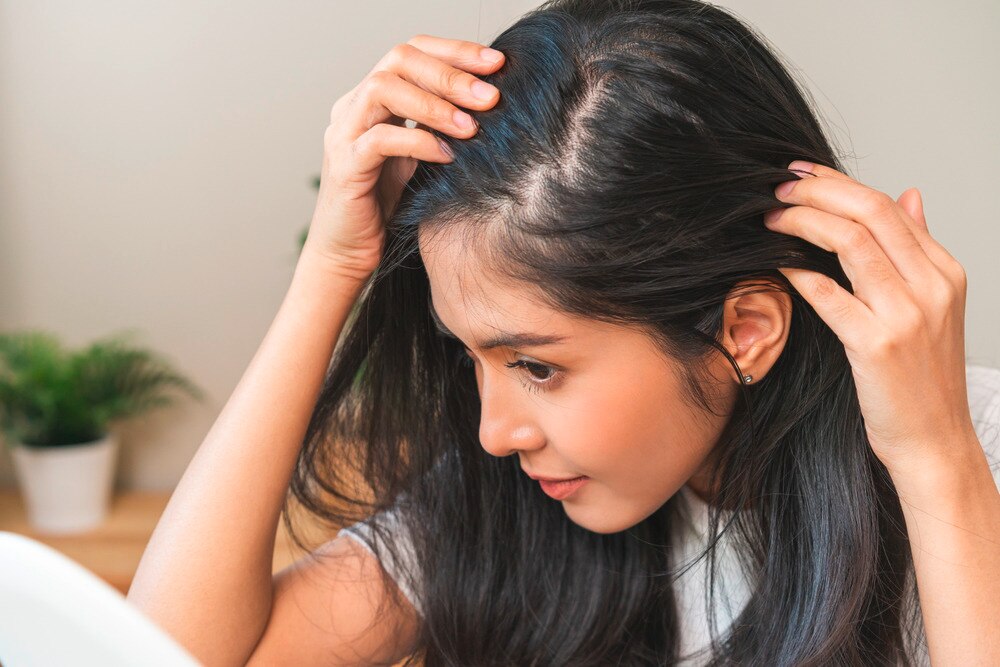A portrait of woman checking her scalp in the mirror.