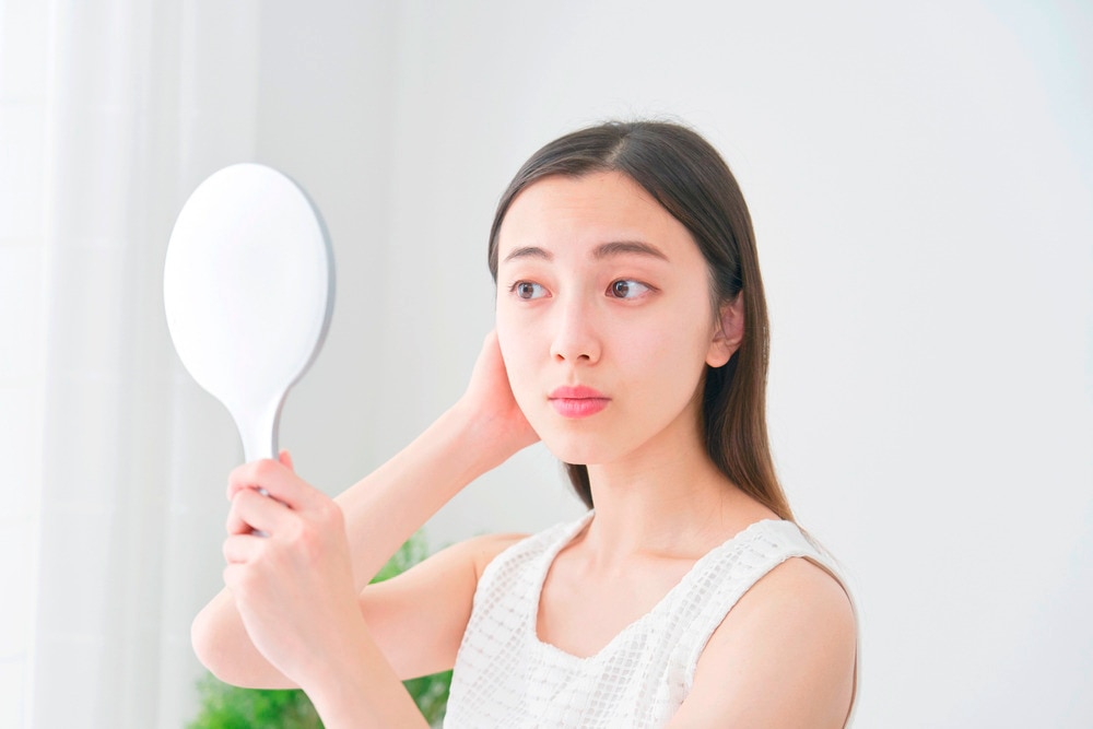 Woman holding a handheld mirror while checking her fine hair.