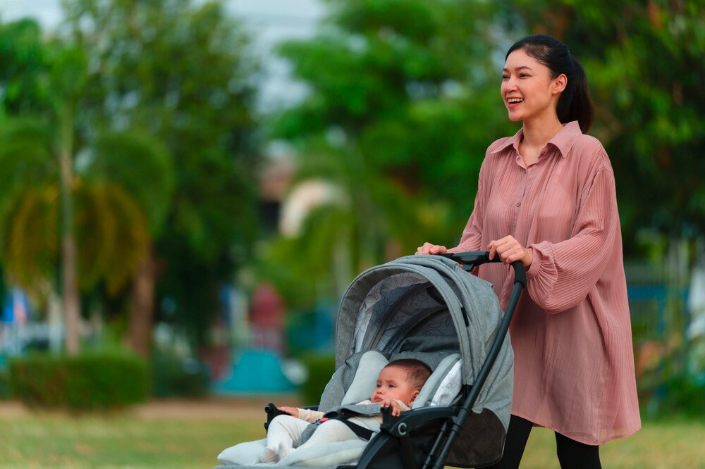 Happy mother pushing baby stroller while walking in the park.