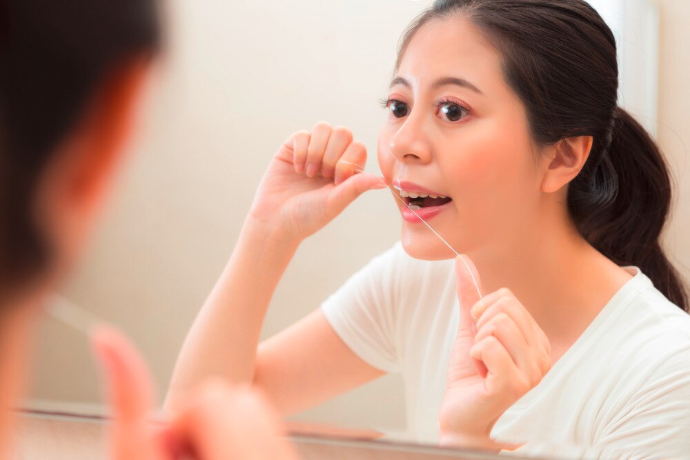 Woman flossing her teeth in the bathroom.