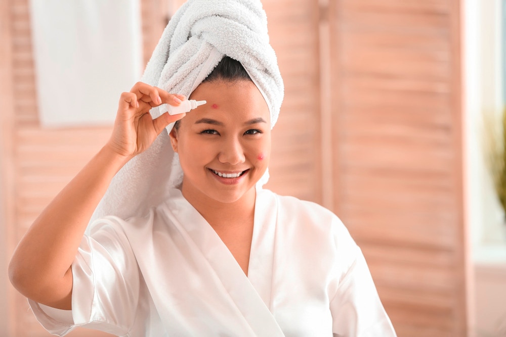 Woman applying acne treatment onto a red bump on her forehead.