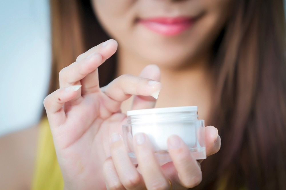 Woman taking a small amount of face cream from the jar.