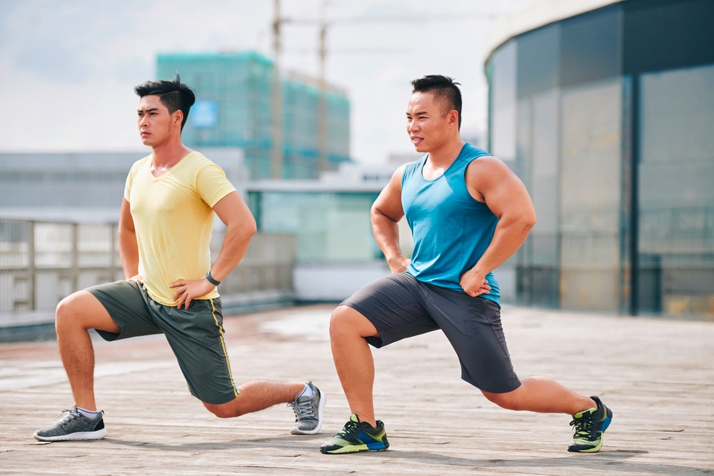 Two men doing lunges together on a rooftop.