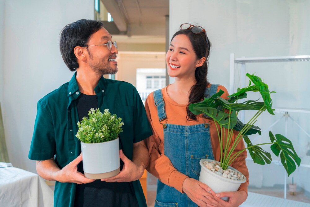 Man and woman holding pots of plant while smiling at each other.