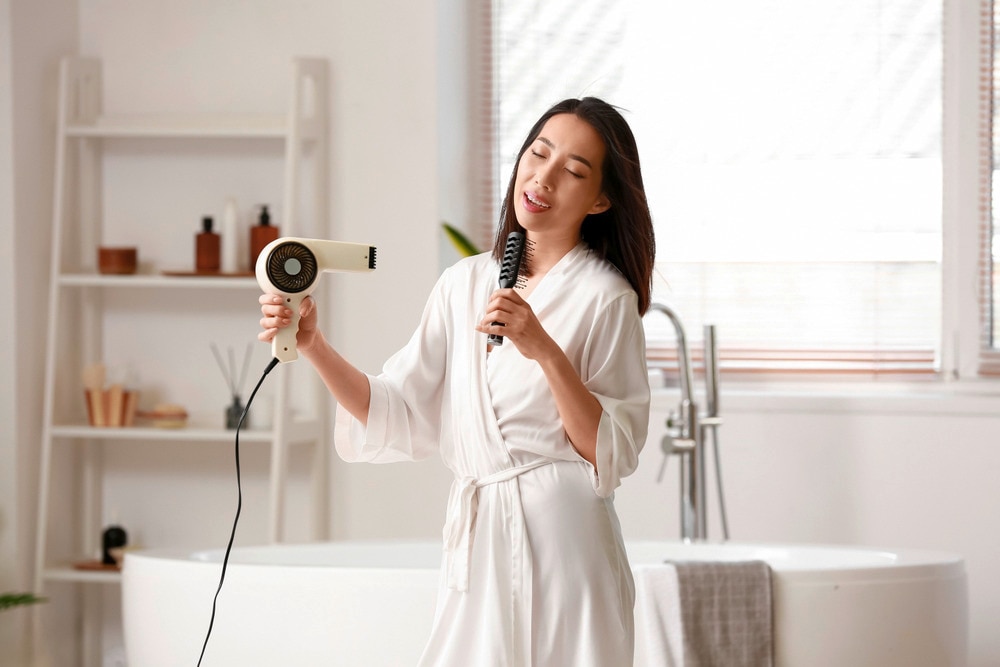 Woman drying hair while singing in bathroom.