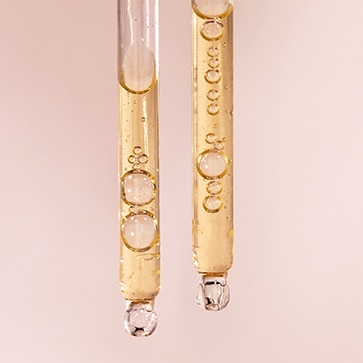 Two glass droppers filled with a light golden serum are shown with small air bubbles inside