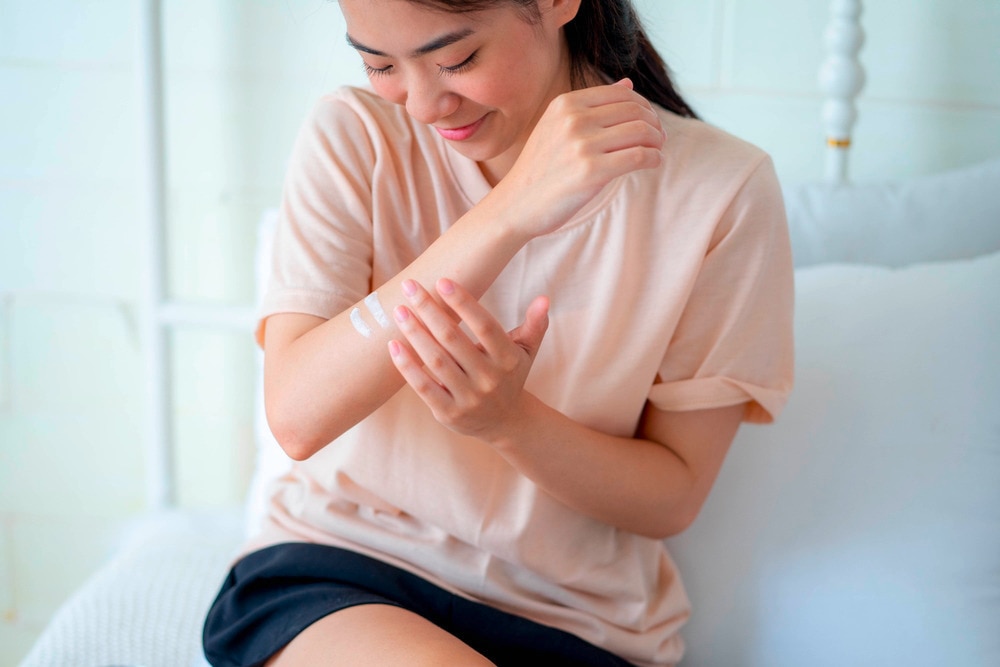 Woman rubbing lotion on her arm.