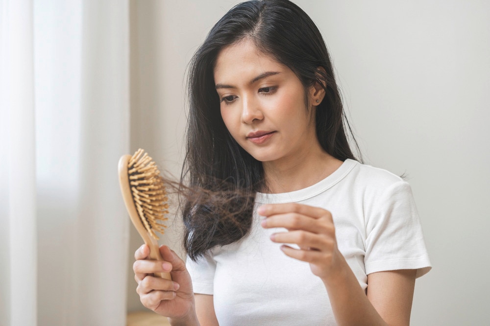 Asian woman looking at hair fall in brush.
