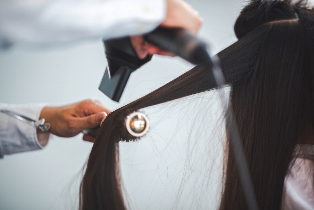 Stylist blow-drying woman’s dark hair.