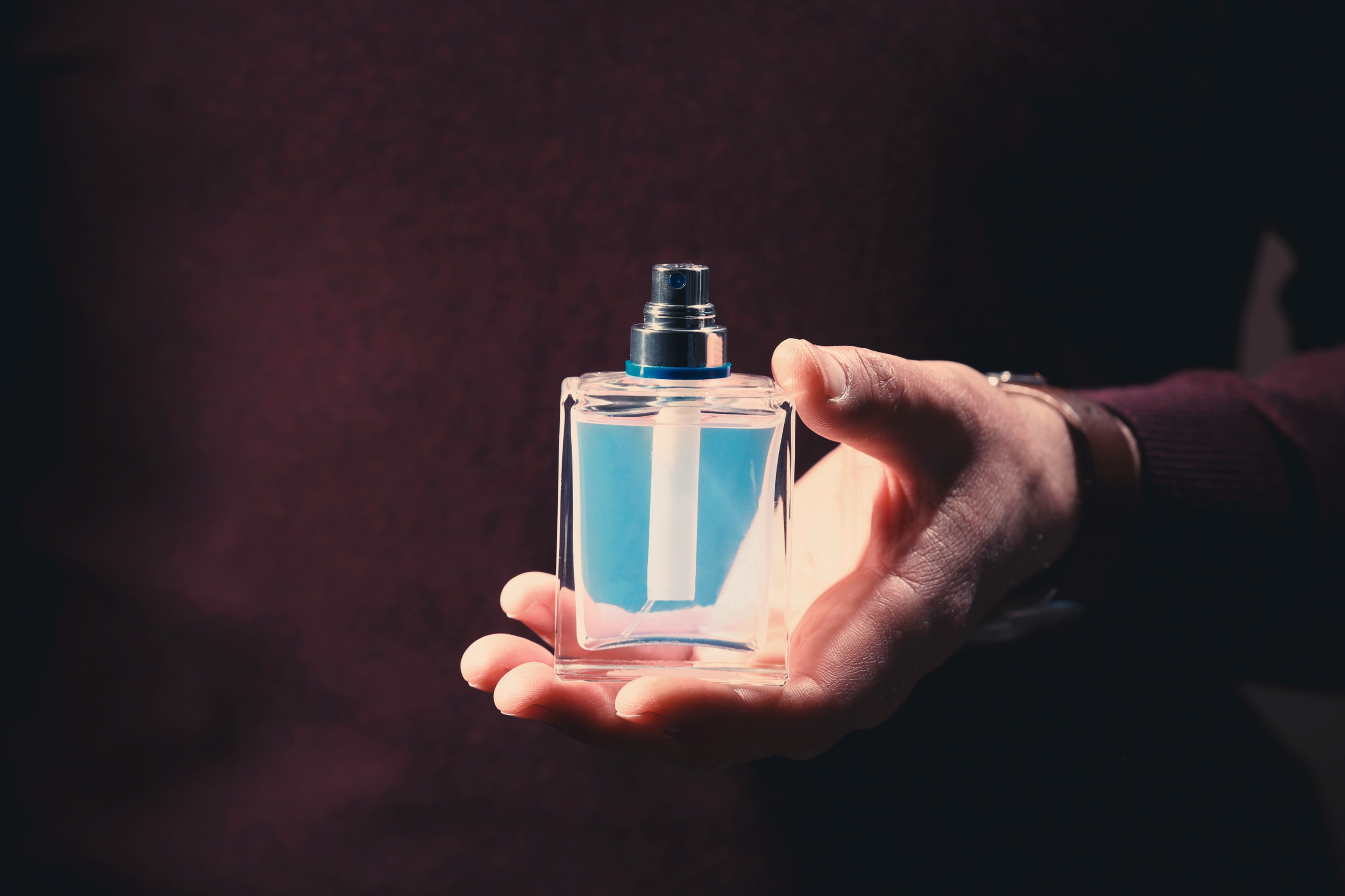 pria sedang memegang botol parfum bening