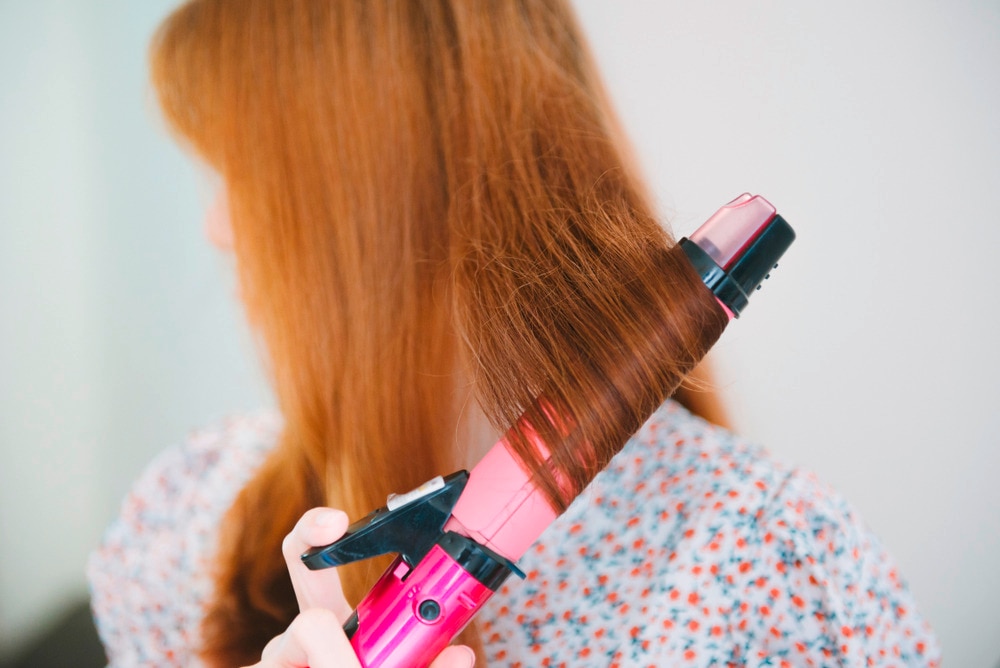 Woman with brassy, damaged hair using curling iron.