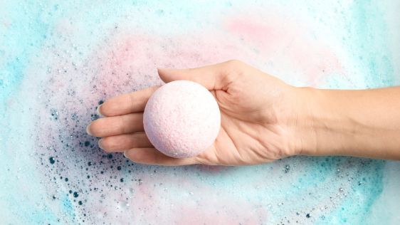 Manicured hand placing a bath bomb into a bathtub filled with water