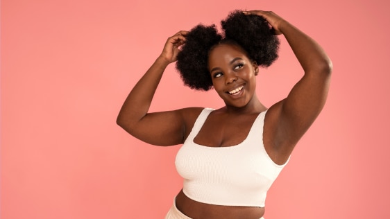 A black woman smiling and raising both hands to touch her hair