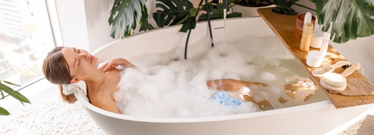 Young woman relaxing in a bathscaped bathtub with headphones on drinking a cup of tea