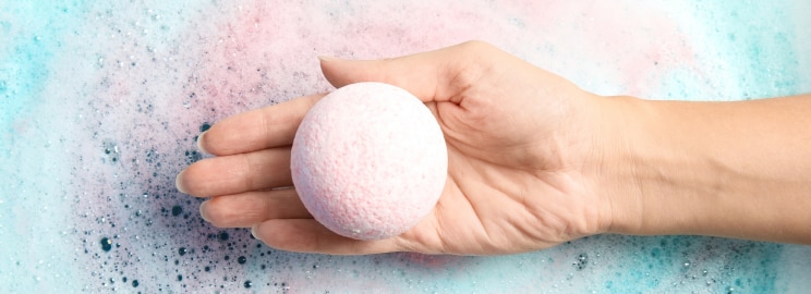 Manicured hand placing a bath bomb into a bathtub filled with water