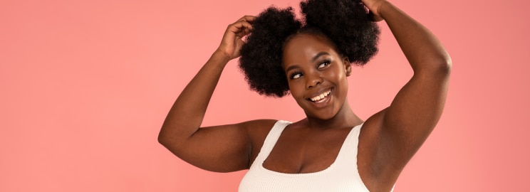 A black woman smiling and raising both hands to touch her hair