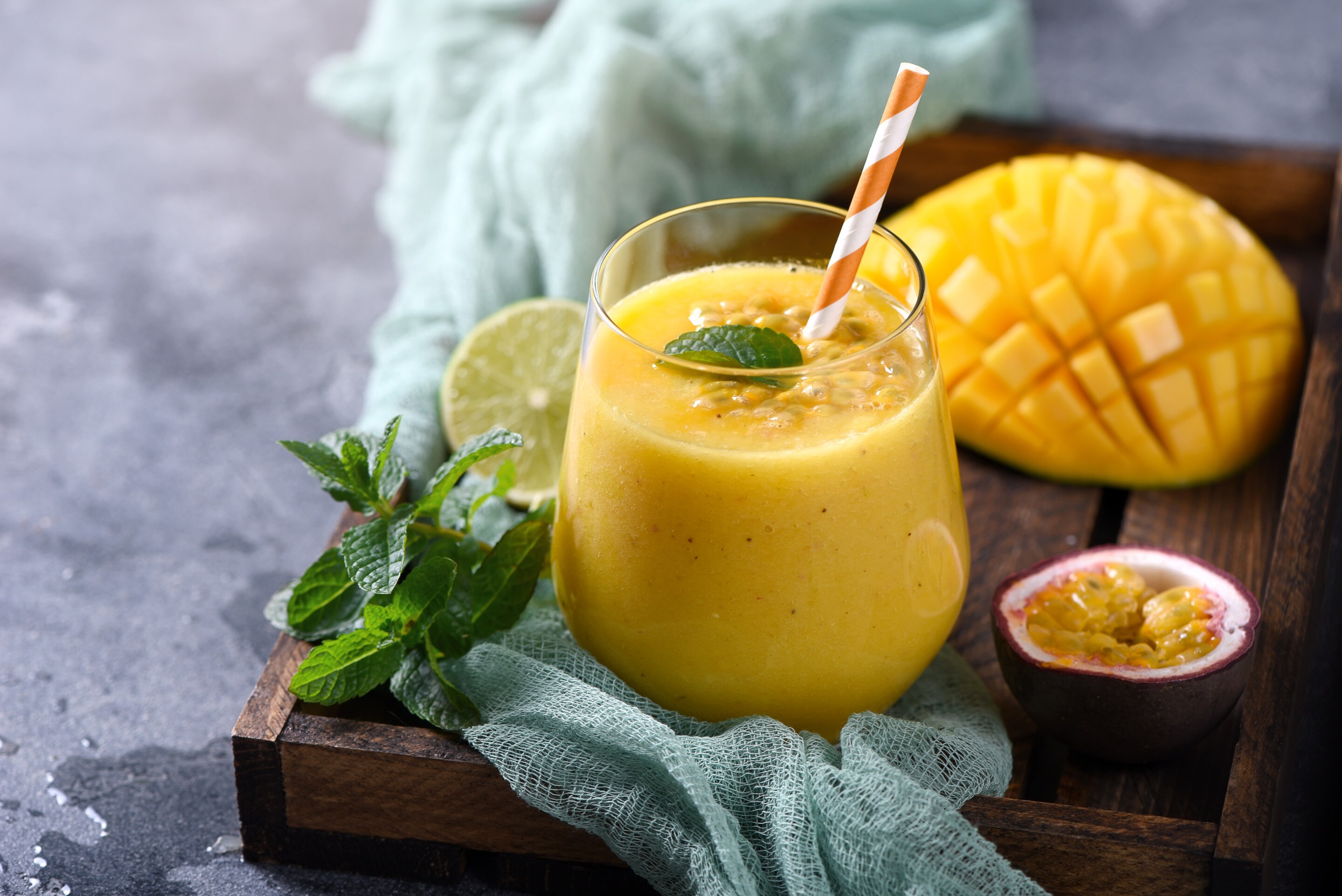 A glass of fresh mango shake with a slice of mango on a wooden tray.