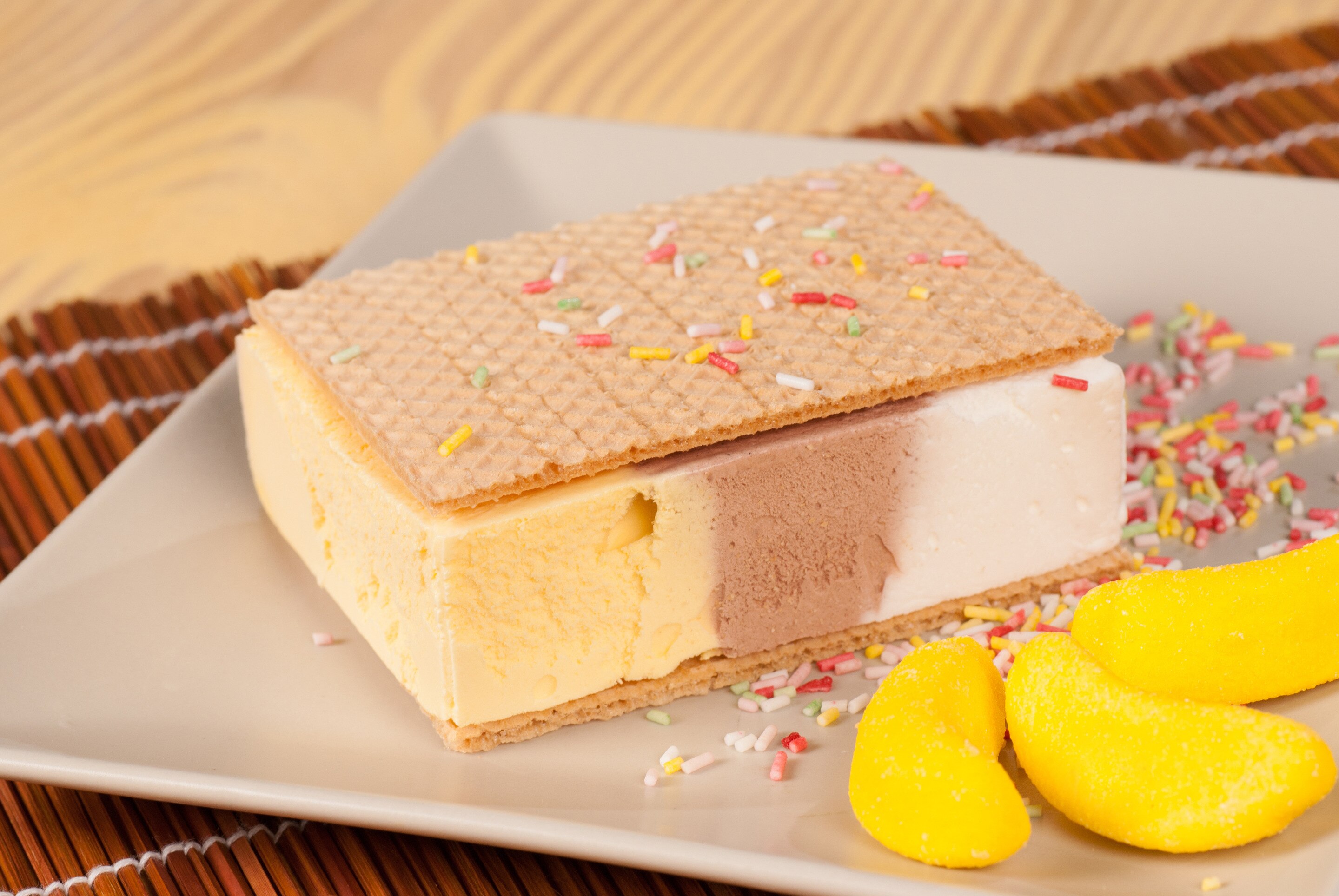 A mango ice cream sandwich with colorful sprinkles on a square plate.