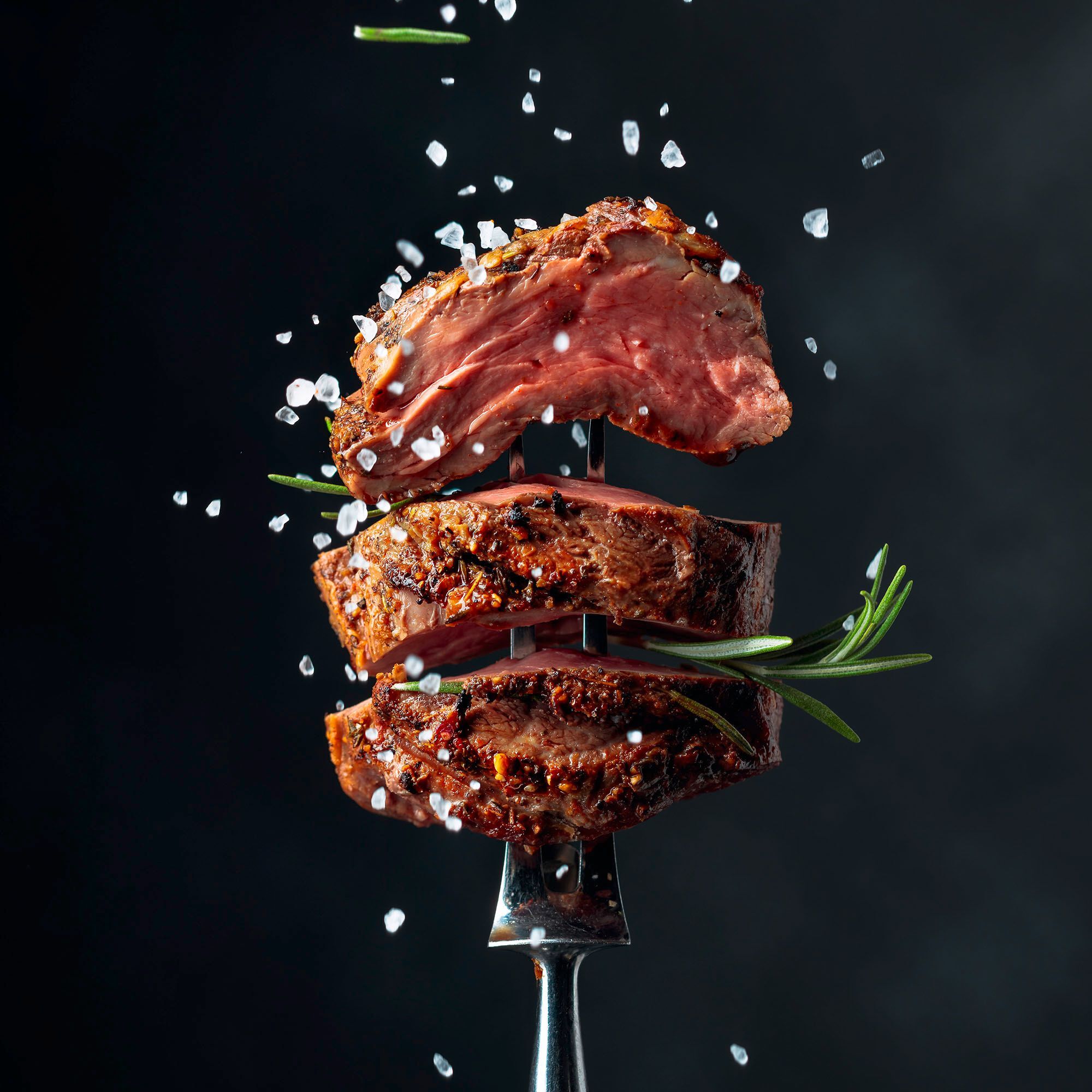 Grilled beef steak on a fork sprinkled with rosemary and sea salt image 3