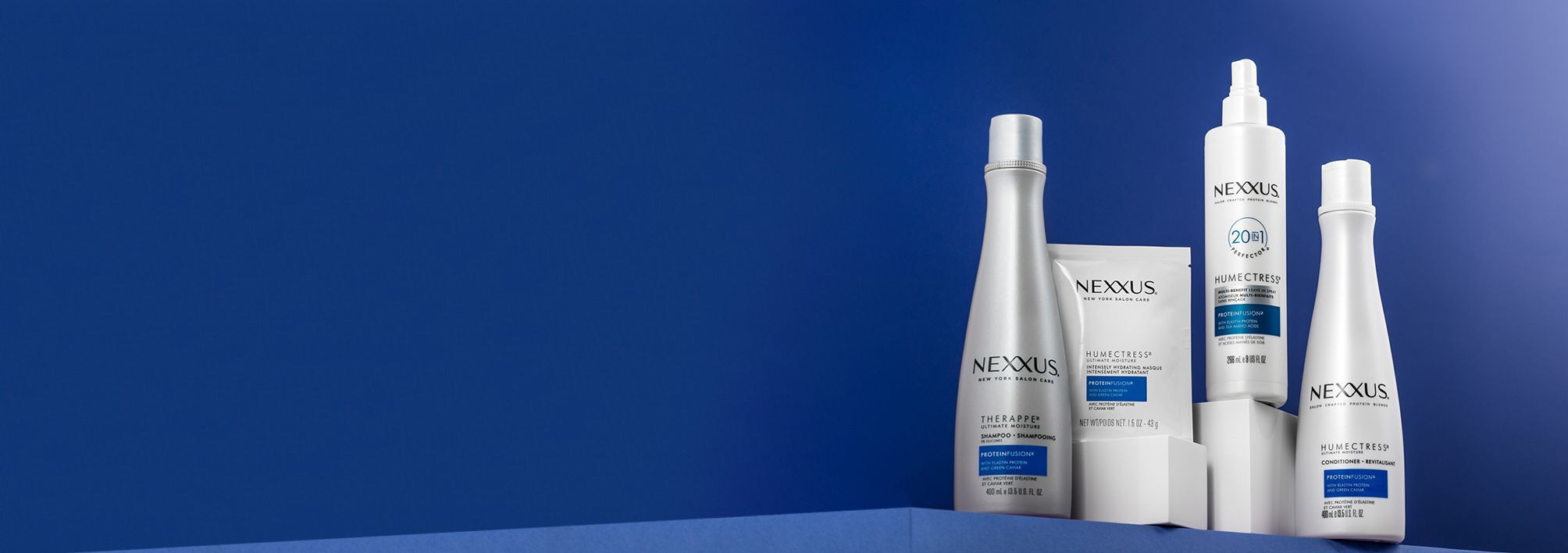 Therappe™ & Humectress™ collection, including bottle of shampoo, bottle of conditioner, hair mask packet, and 20-in-1 multi-benefit leave-in conditioner spray bottle, shown against a blue background.