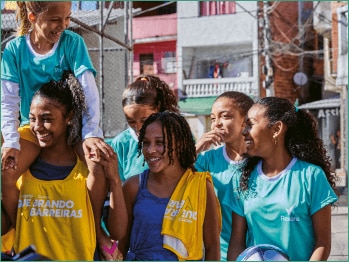 Garotas entre um campo e algumas casas sorrindo