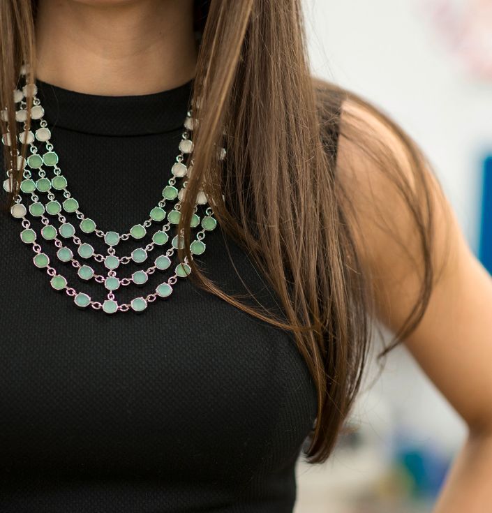 Closeup shot of a woman wearing a black top wearing a green necklace with her hand on her hip