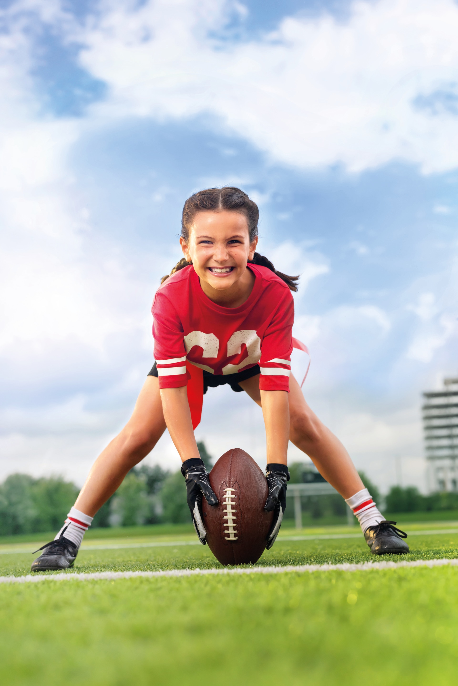 Girl smiling holding a football between her feet on a football field