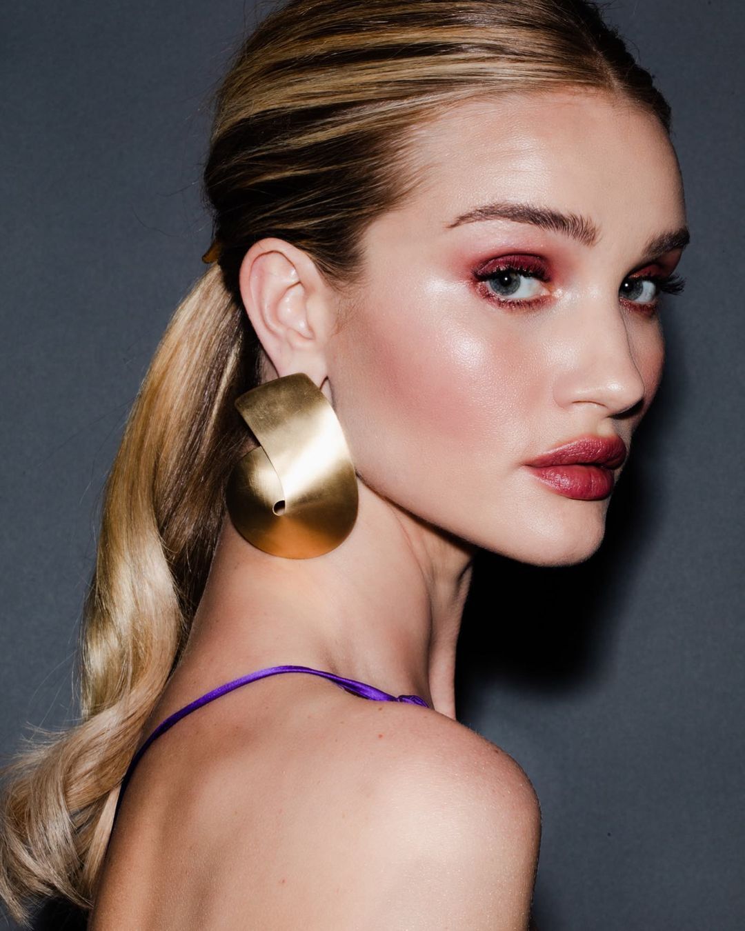 Rosie Huntington Whiteley wearing golden earrings and a low ponytail. 