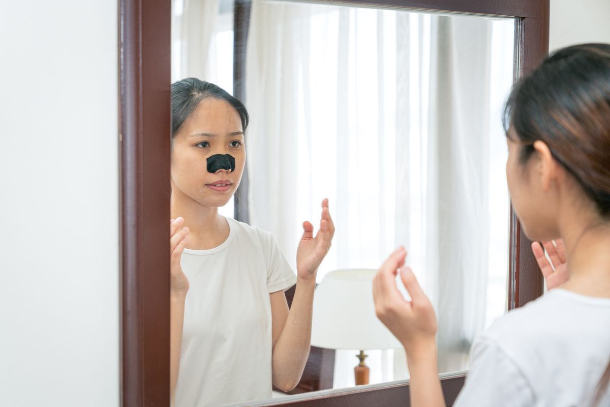 Woman using a black nose strip in front of a mirror.