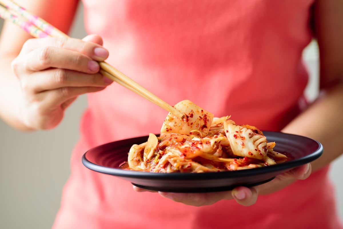 Woman holding chopsticks and a plate of kimchi. 