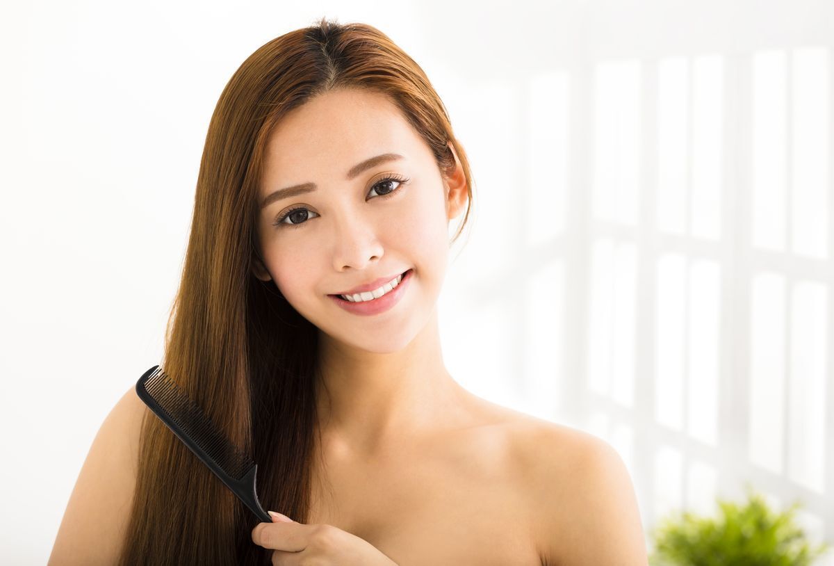 Woman brushing her long hair with a black comb.