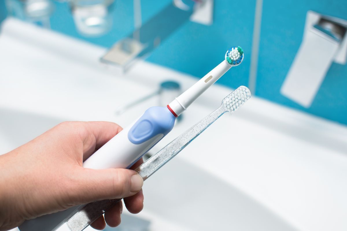  A hand holding an electric toothbrush and a manual toothbrush. 