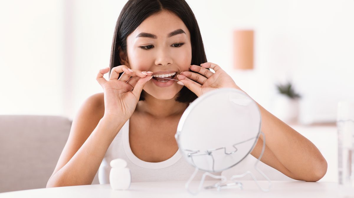 An Asian woman flossing in front of a mirror.
