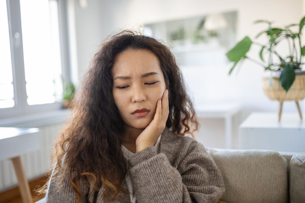 Woman with curly hair touching her cheek in pain from toothache.