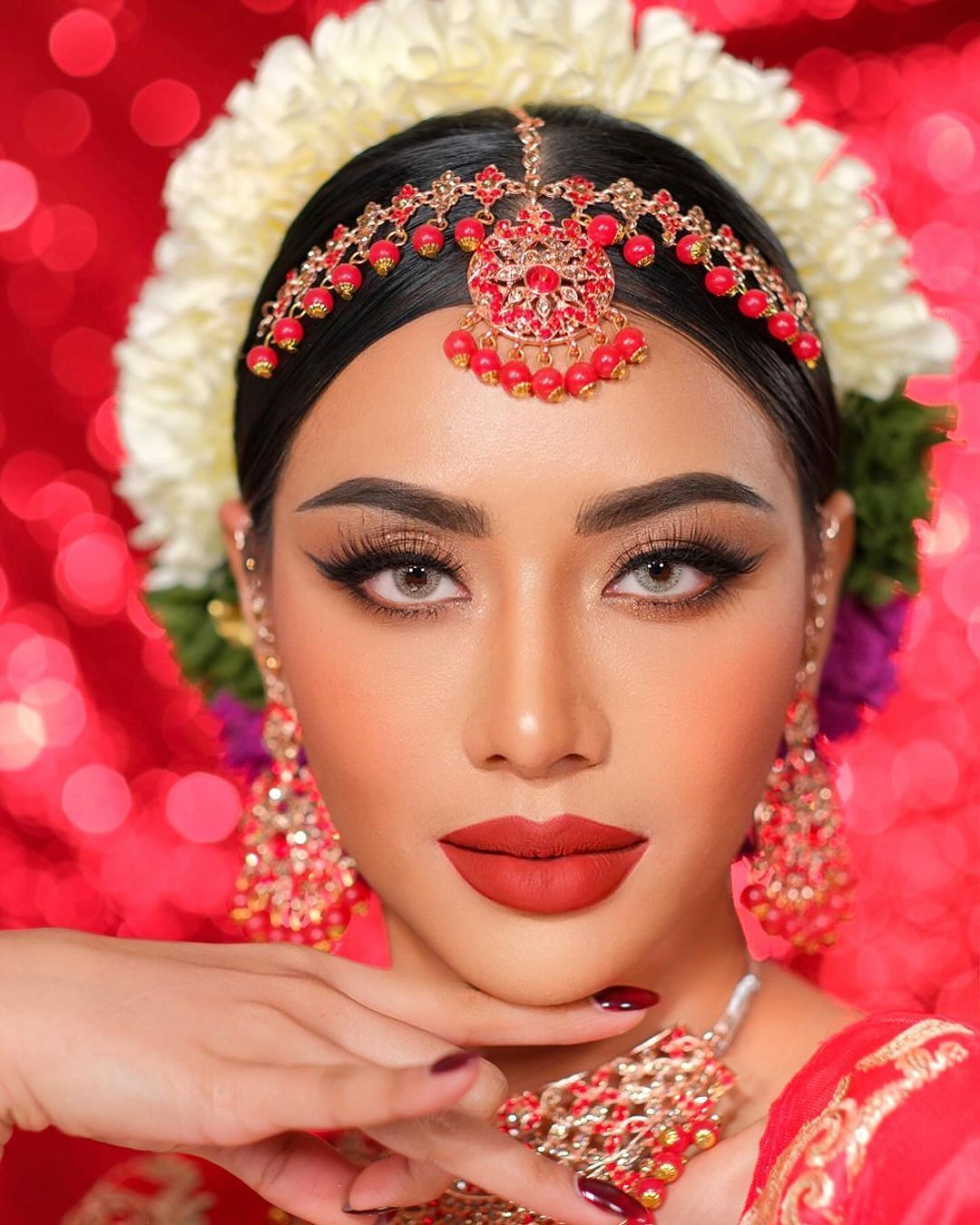 A photo of woman with Gajra, red and golden accessories, and bold makeup.