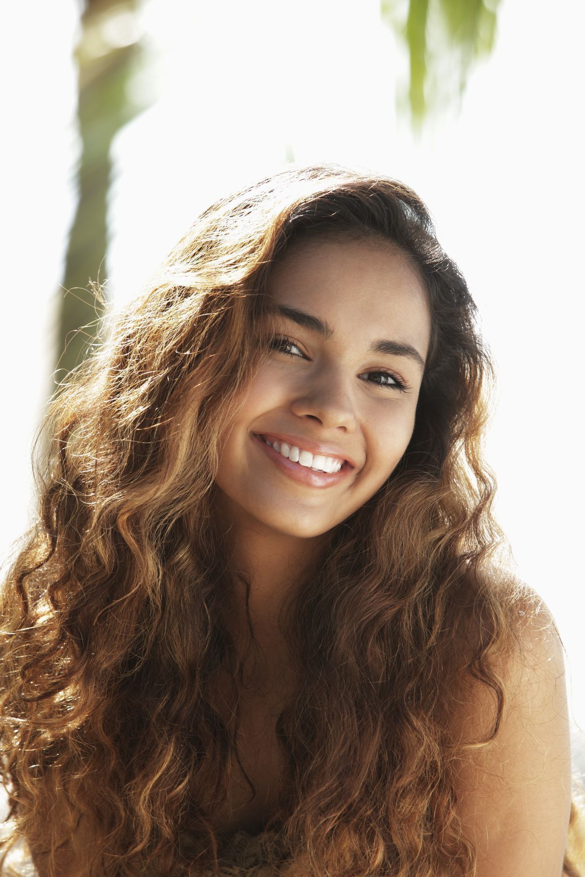 Portrait of an Asian girl smiling with long wavy brown hair outdoors. 