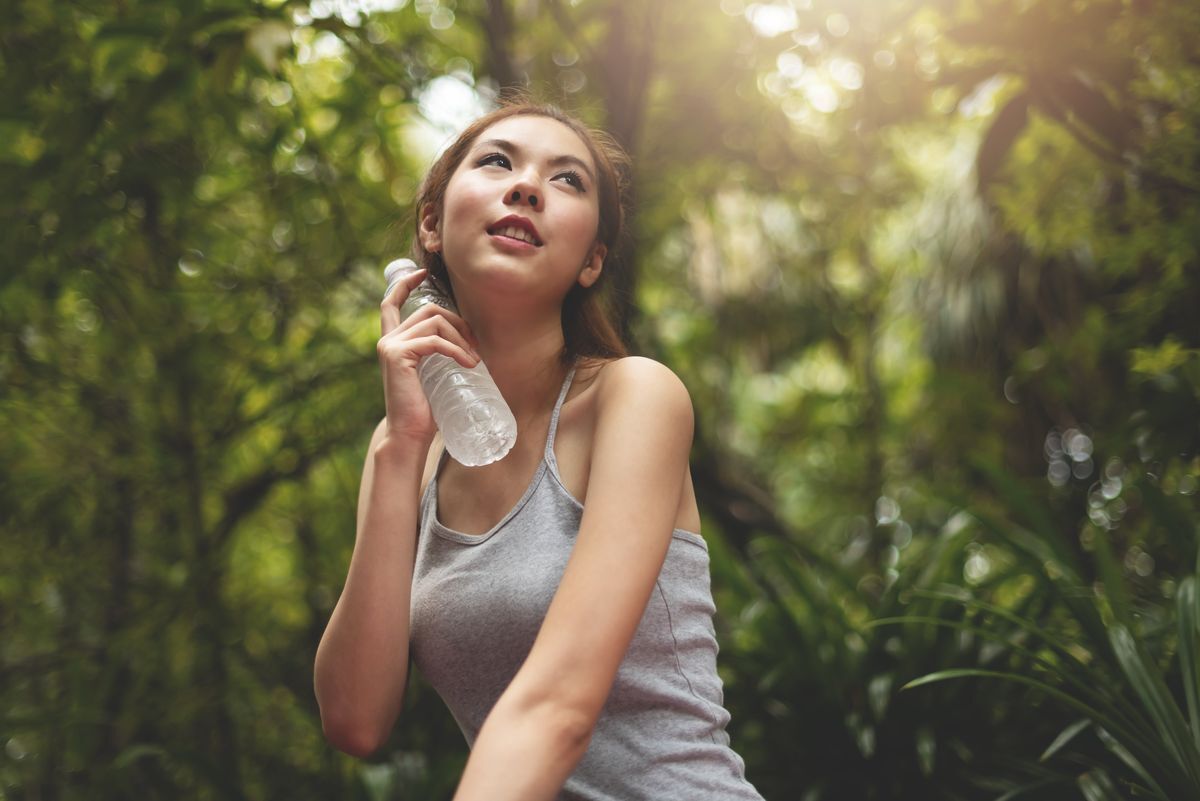 Woman looking up and holding a cold water bottle to her neck.