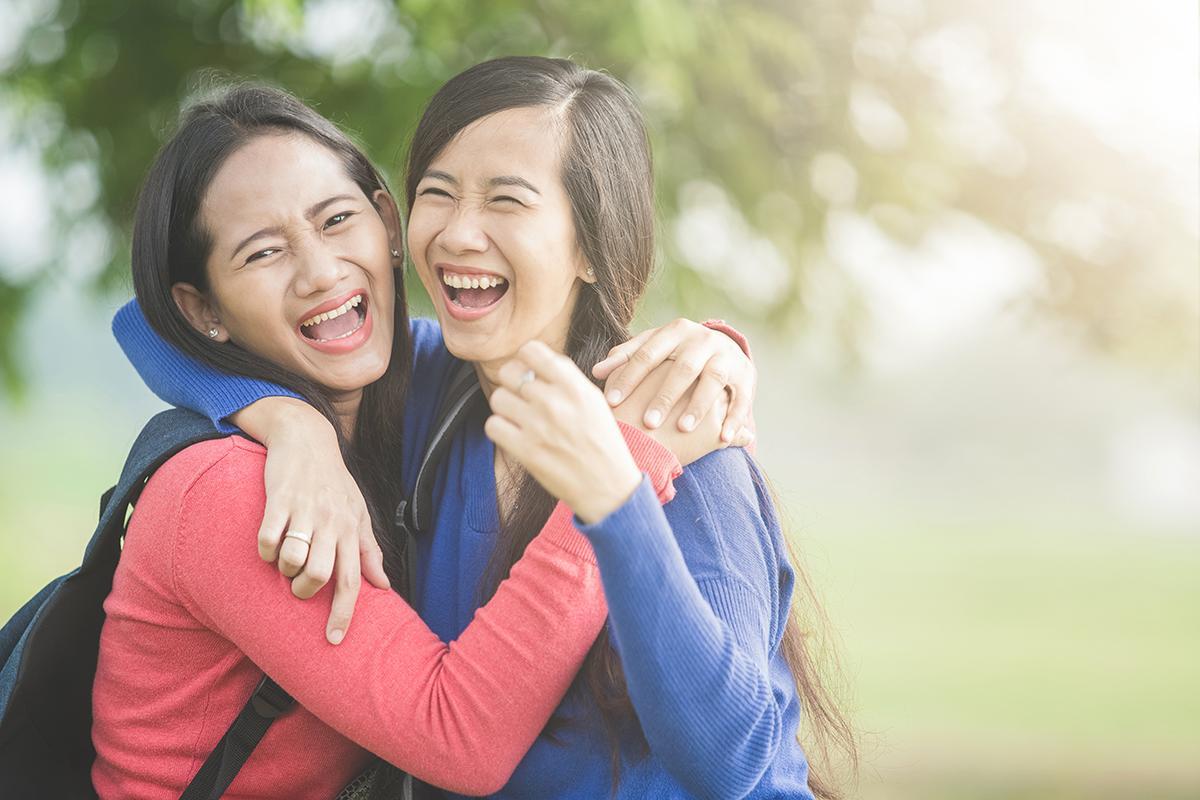 Two Asian women in pink and blue laughing and hugging each other