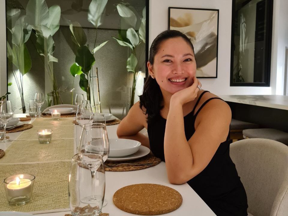 A woman in black dress seated before a dinner table.